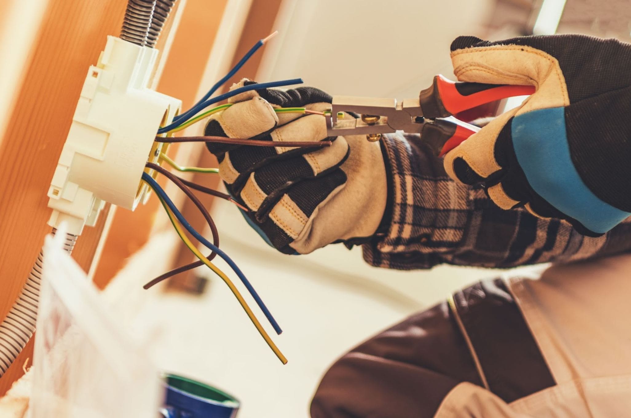 A close-up of an electrician’s gloved hands rewiring colorful cables during electric outlet installation.